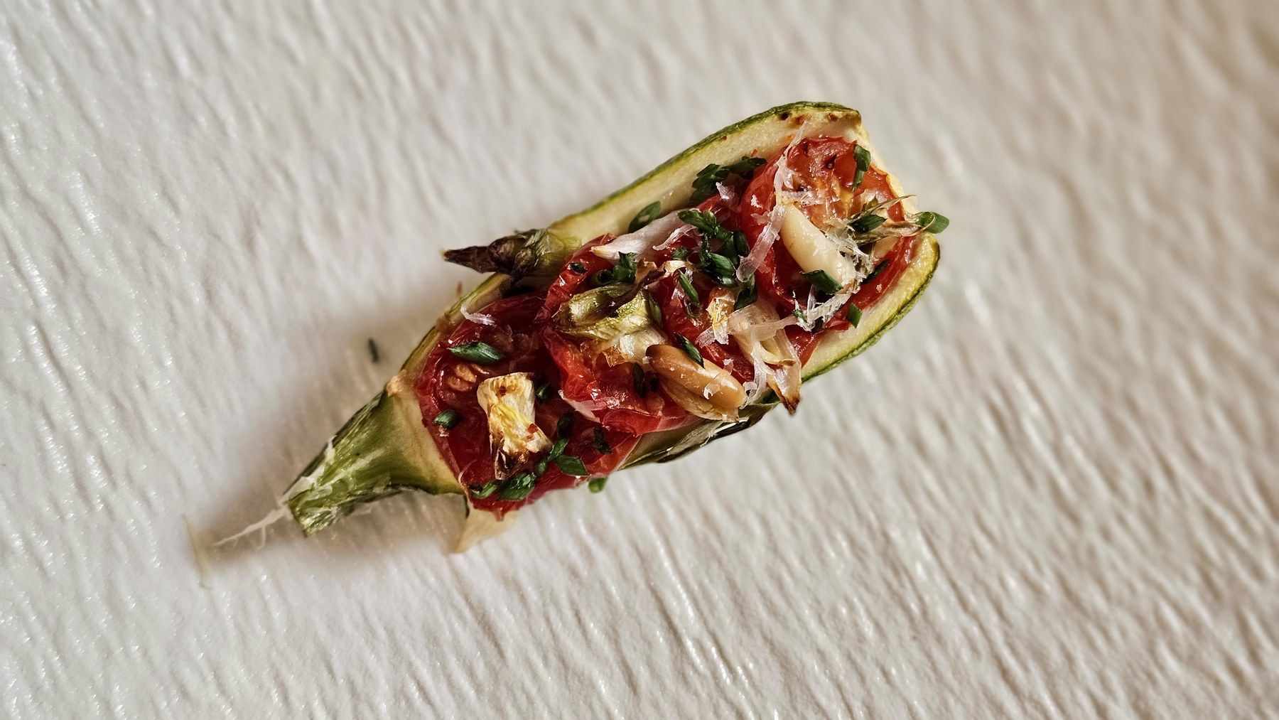Stuffed baby-courgette amuse-bouche on textured porcelain.