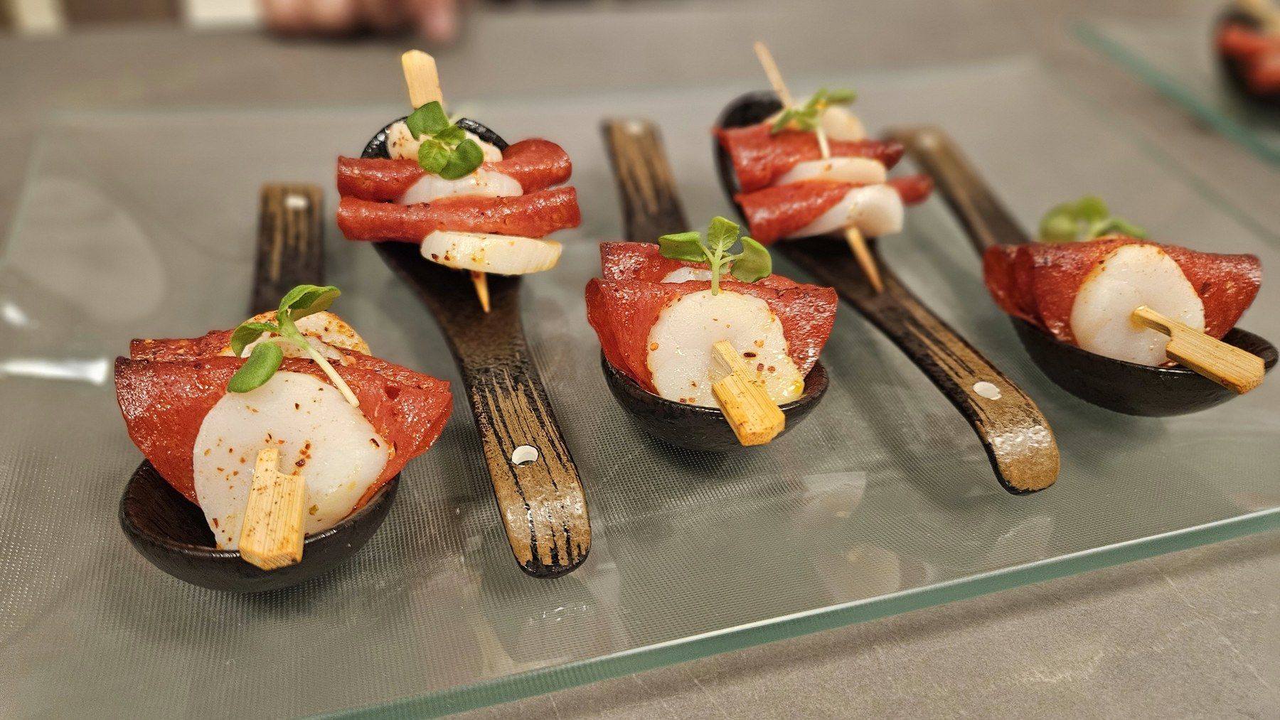 Apéritif bites lined up on serving spoons.