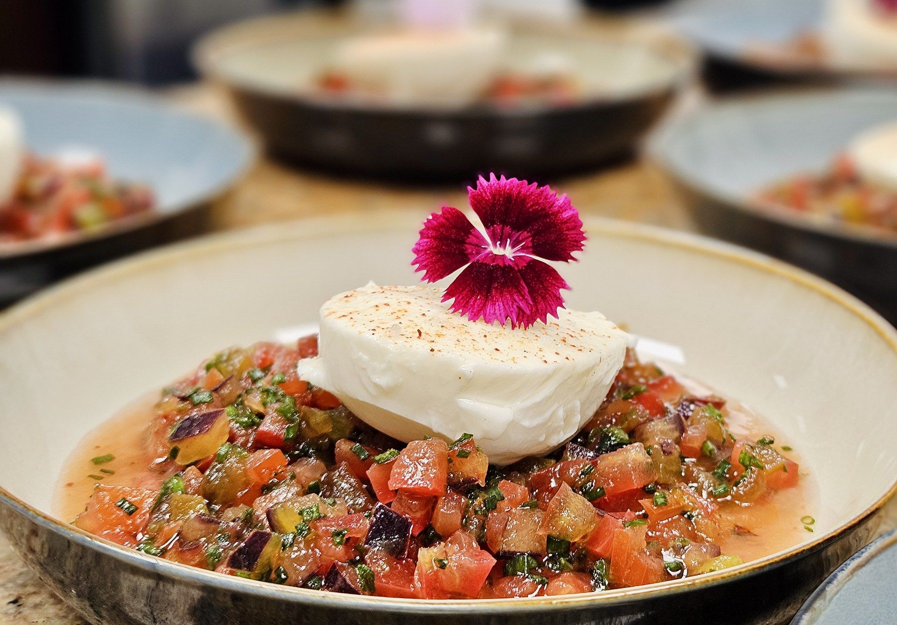 Creamy burrata over a tomato concassé, topped with a dianthus flower.