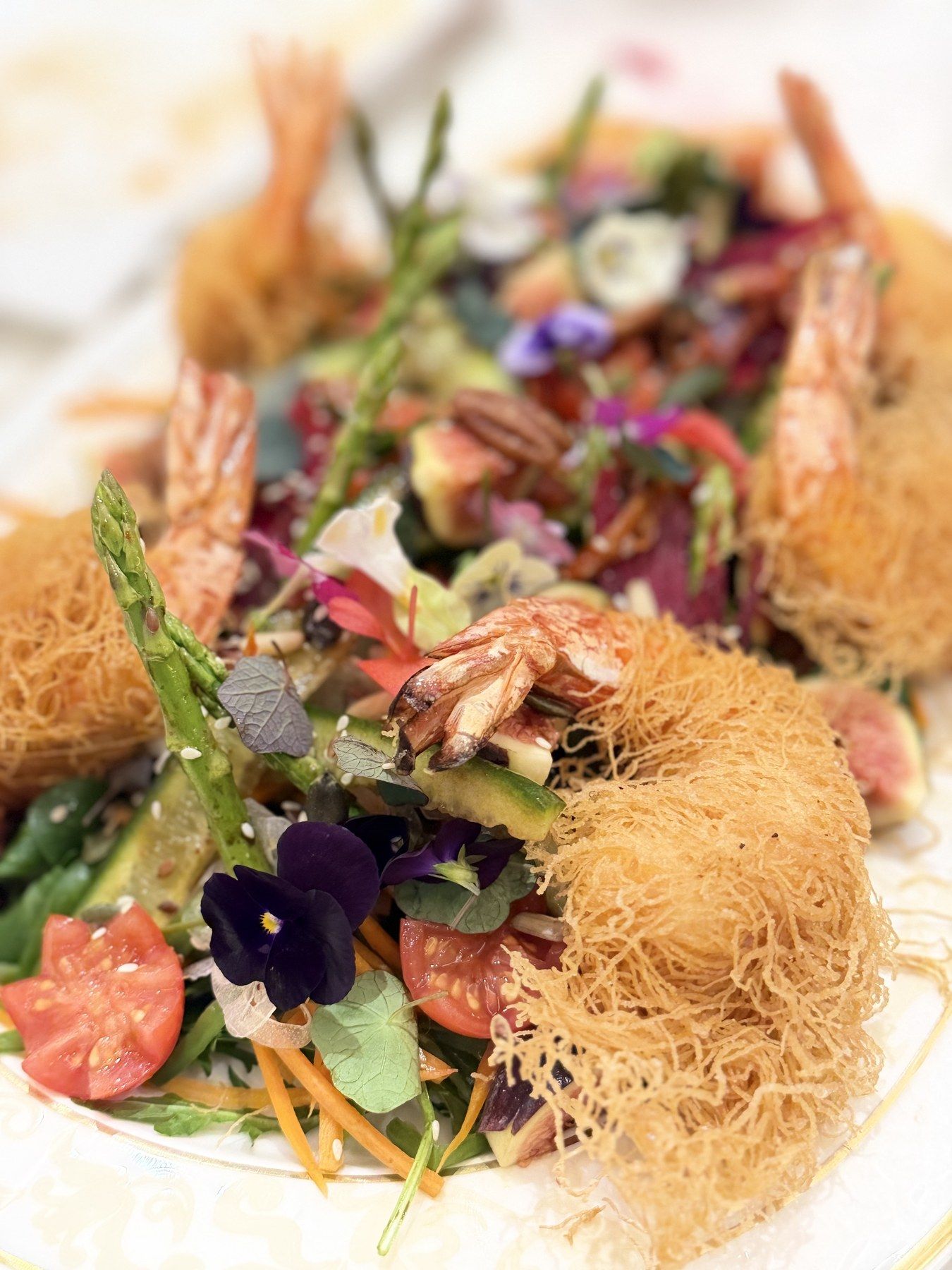 Crispy kadaif prawns over a flowered salad platter.