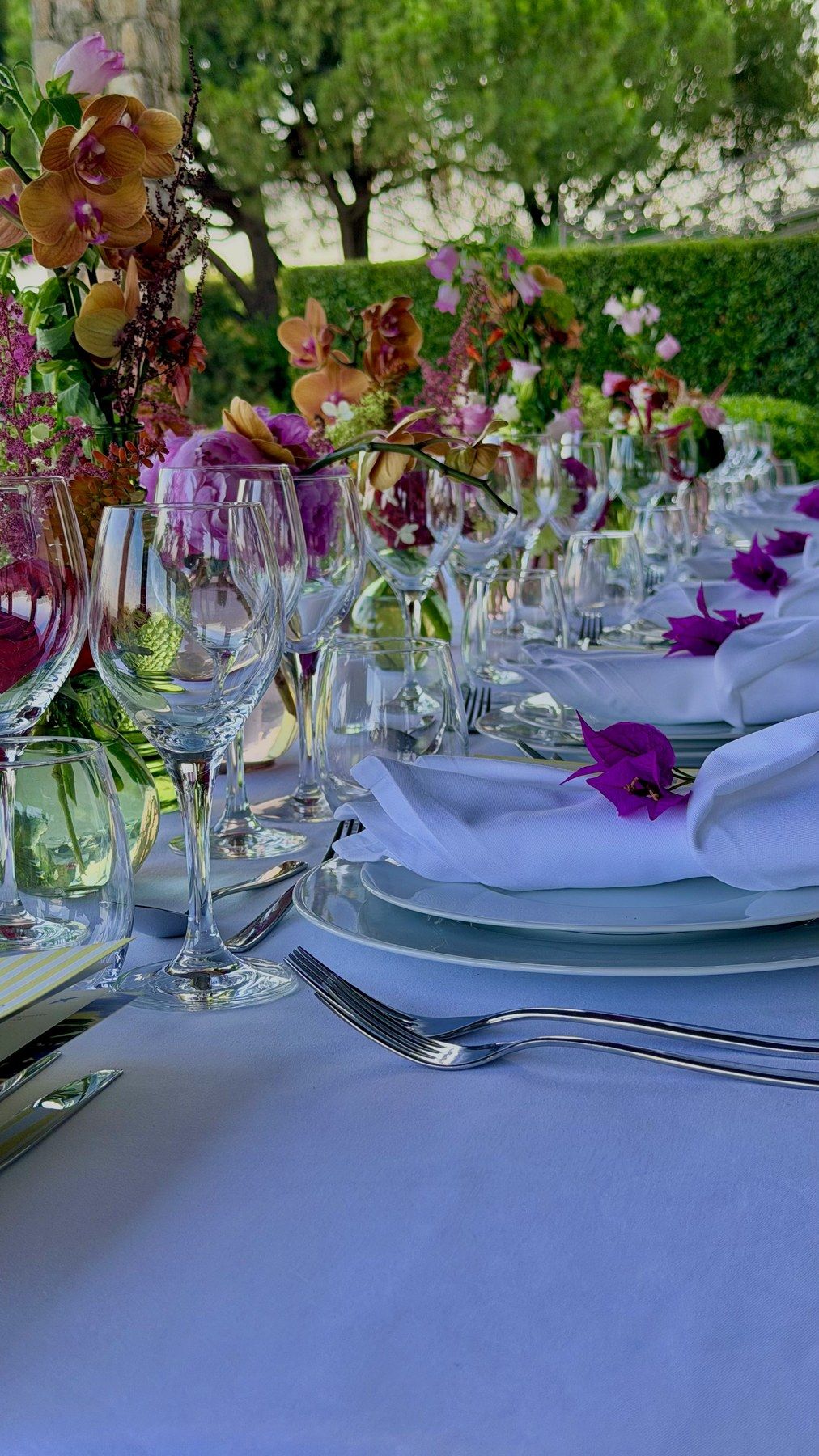 Glassware and vivid florals on a lavender-linen table.