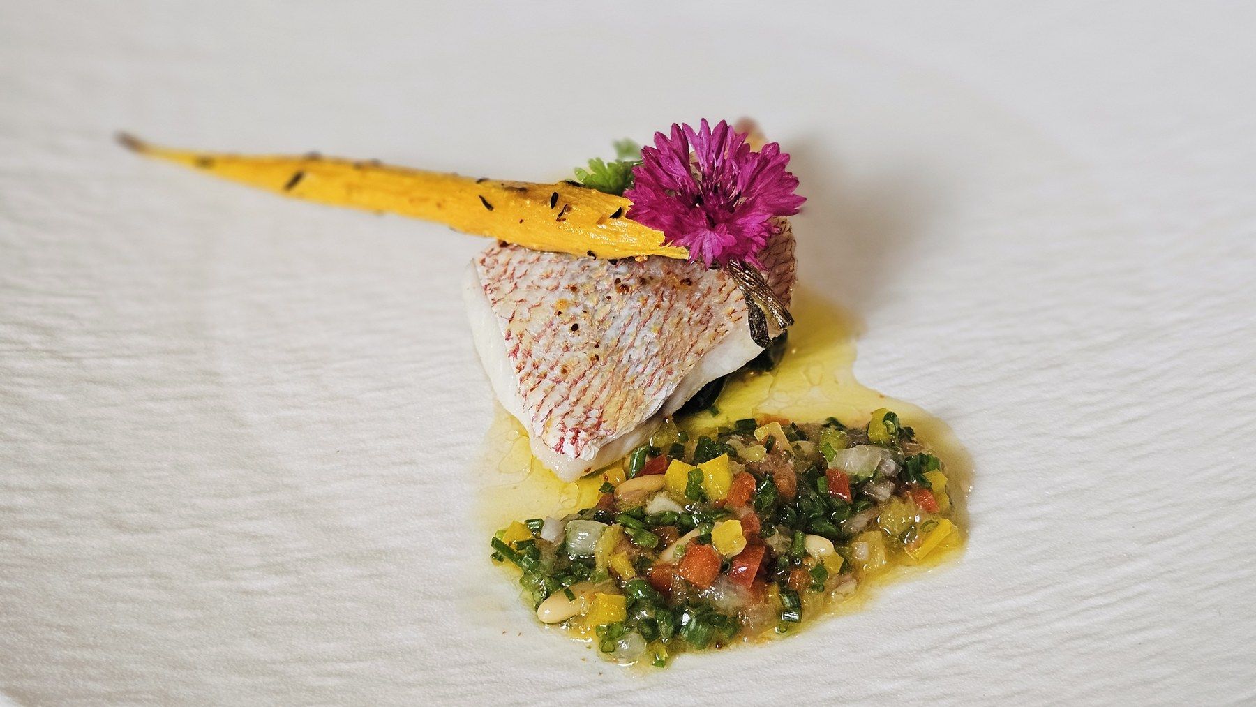 Seared fish fillet on a fine vegetable condiment, carrot crisp and edible flower.