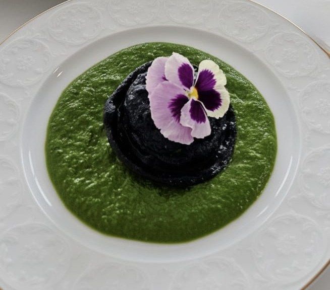 Black galette on a green herb coulis, topped with a pansy.