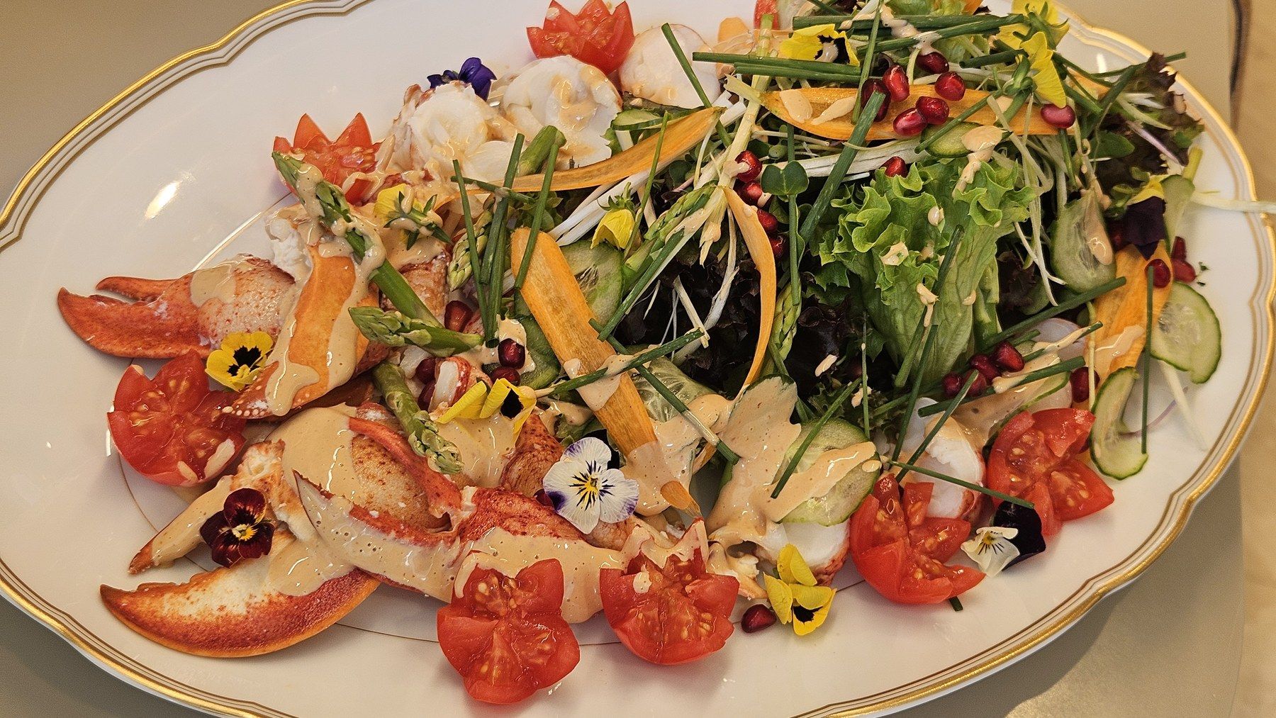 Lobster salad with tomatoes and edible flowers on a gold-rimmed platter.