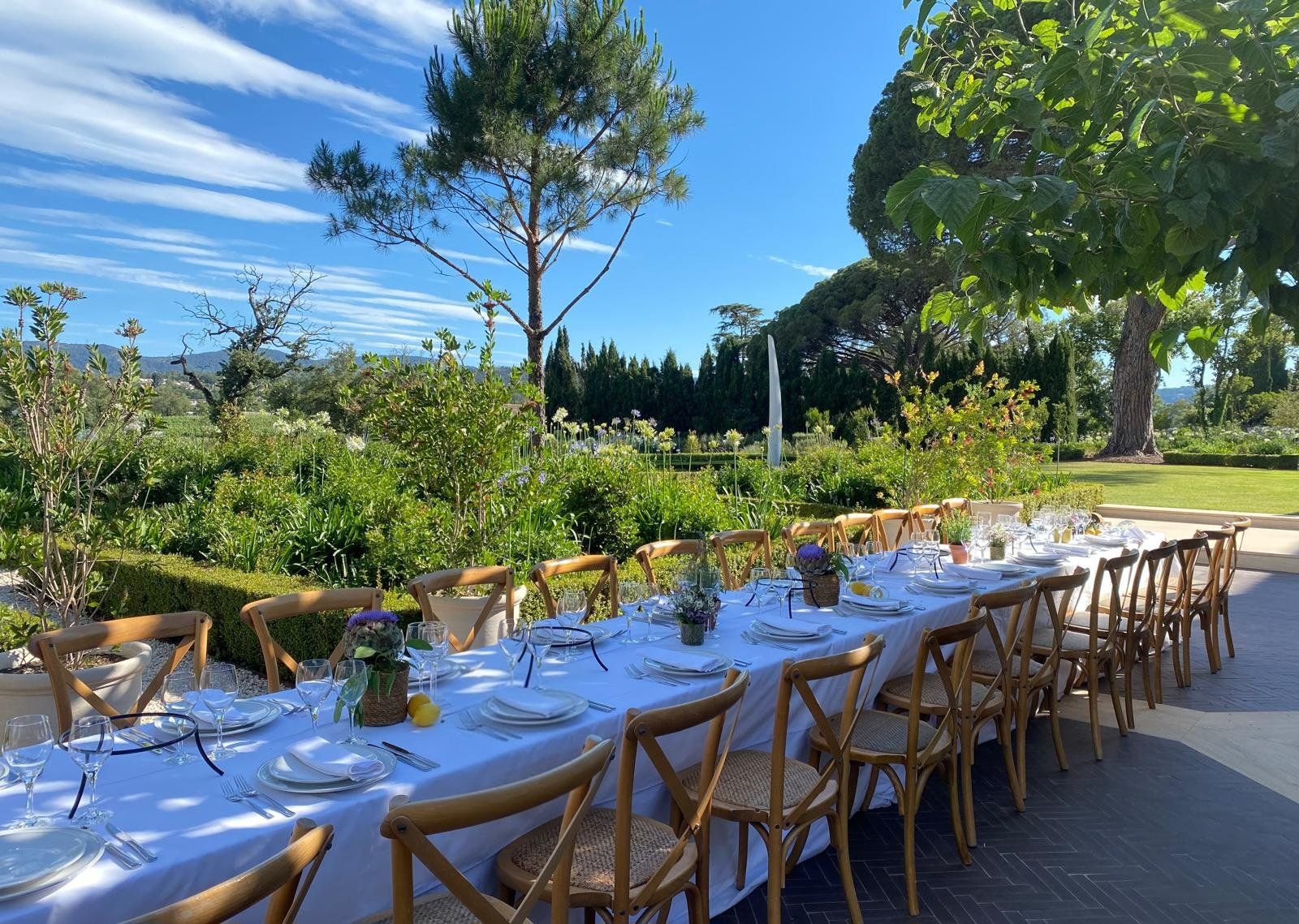 Long villa-terrace banquet table dressed in white linen, bistro chairs and a Provençal garden behind.