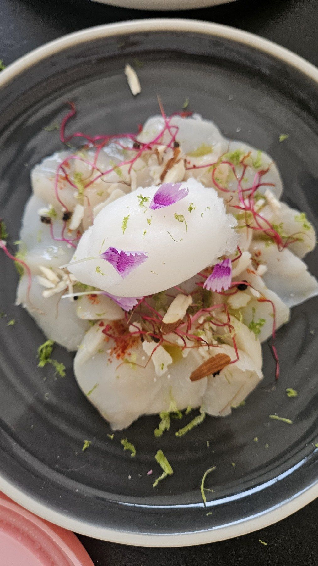 White fish plated with fresh condiments and an edible flower on a dark plate.
