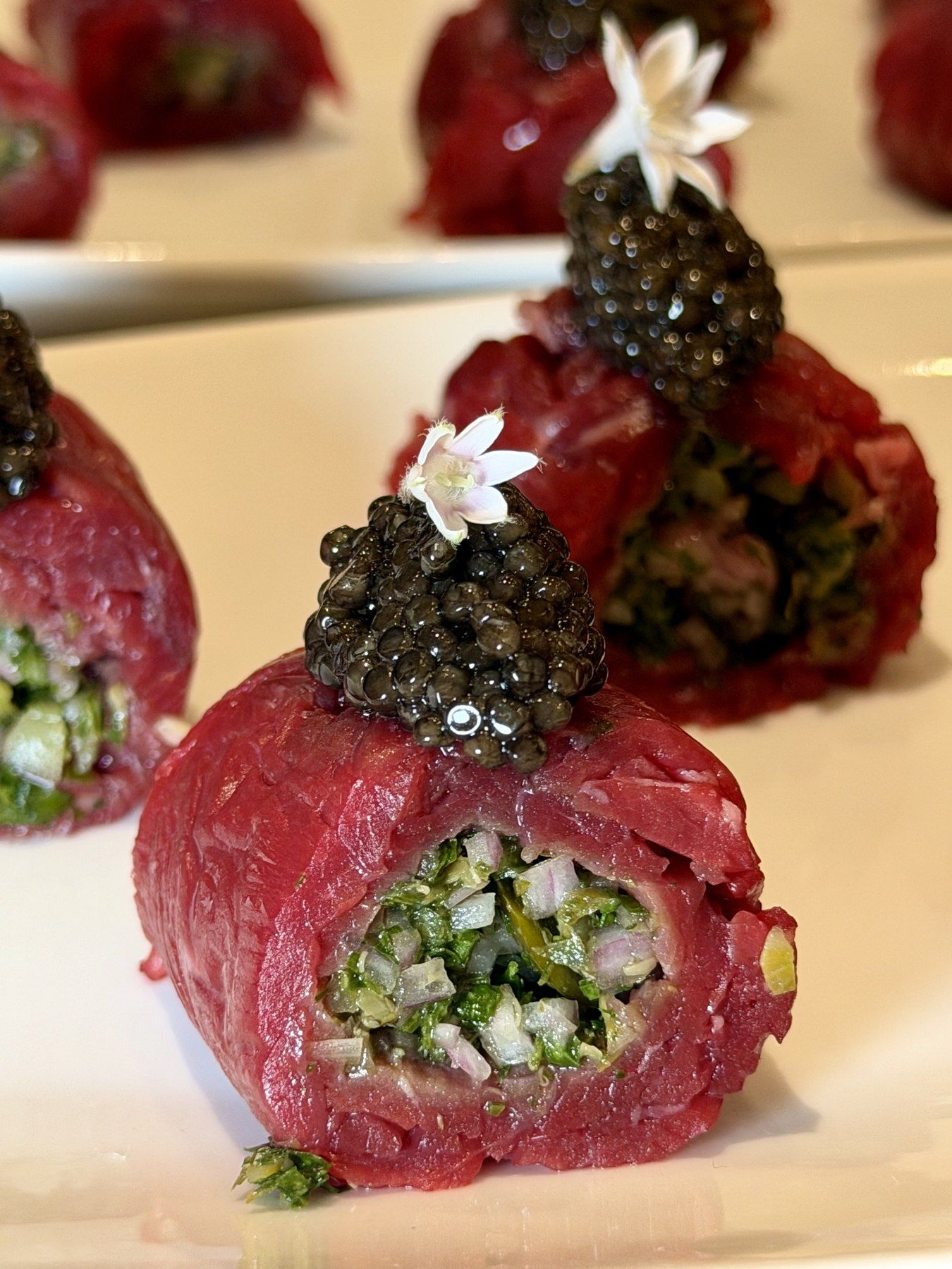 Close-up of a carpaccio roll crowned with caviar and a white flower.