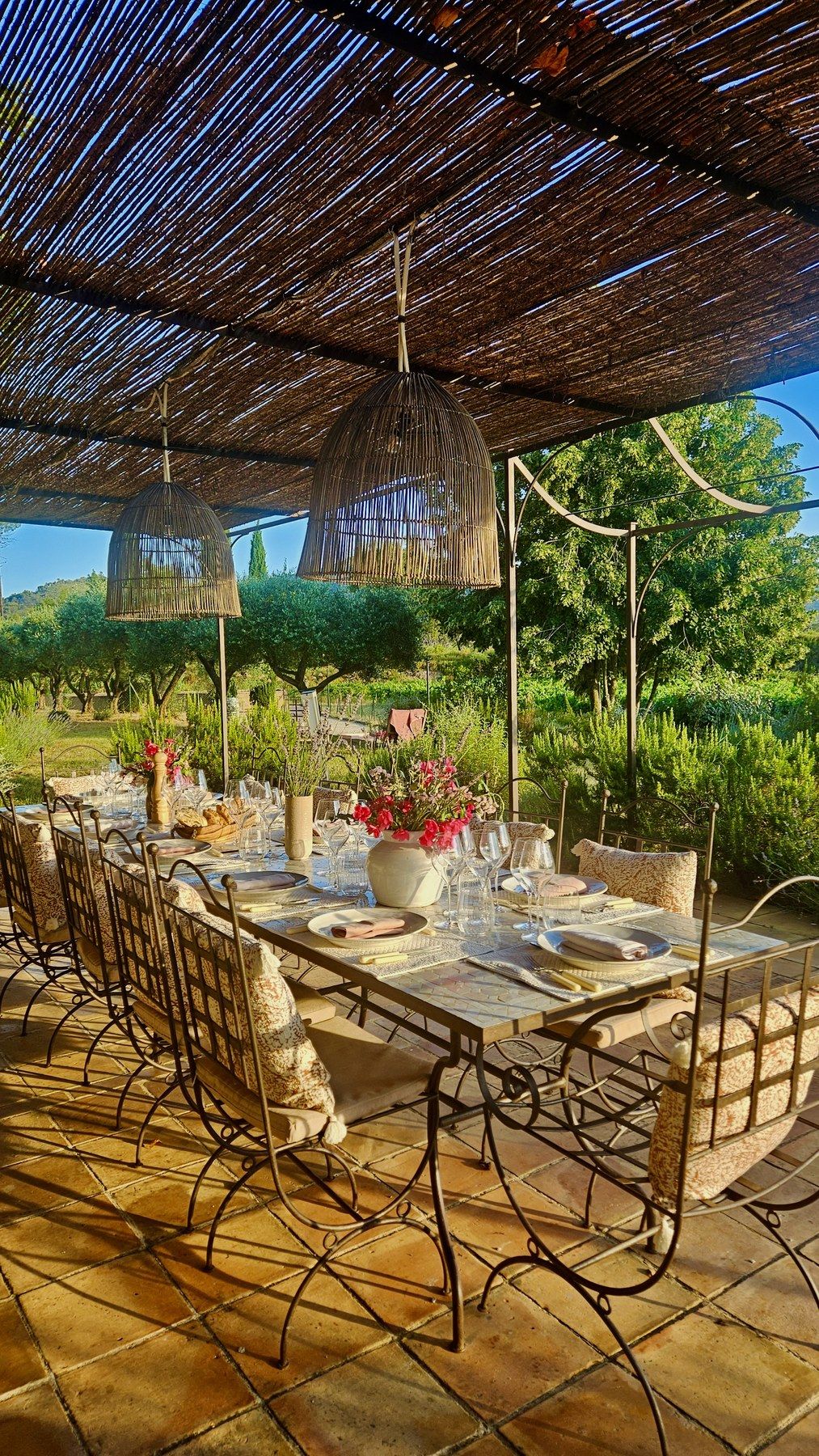 Table dressed on a terrace under a reed canopy, summer evening light.