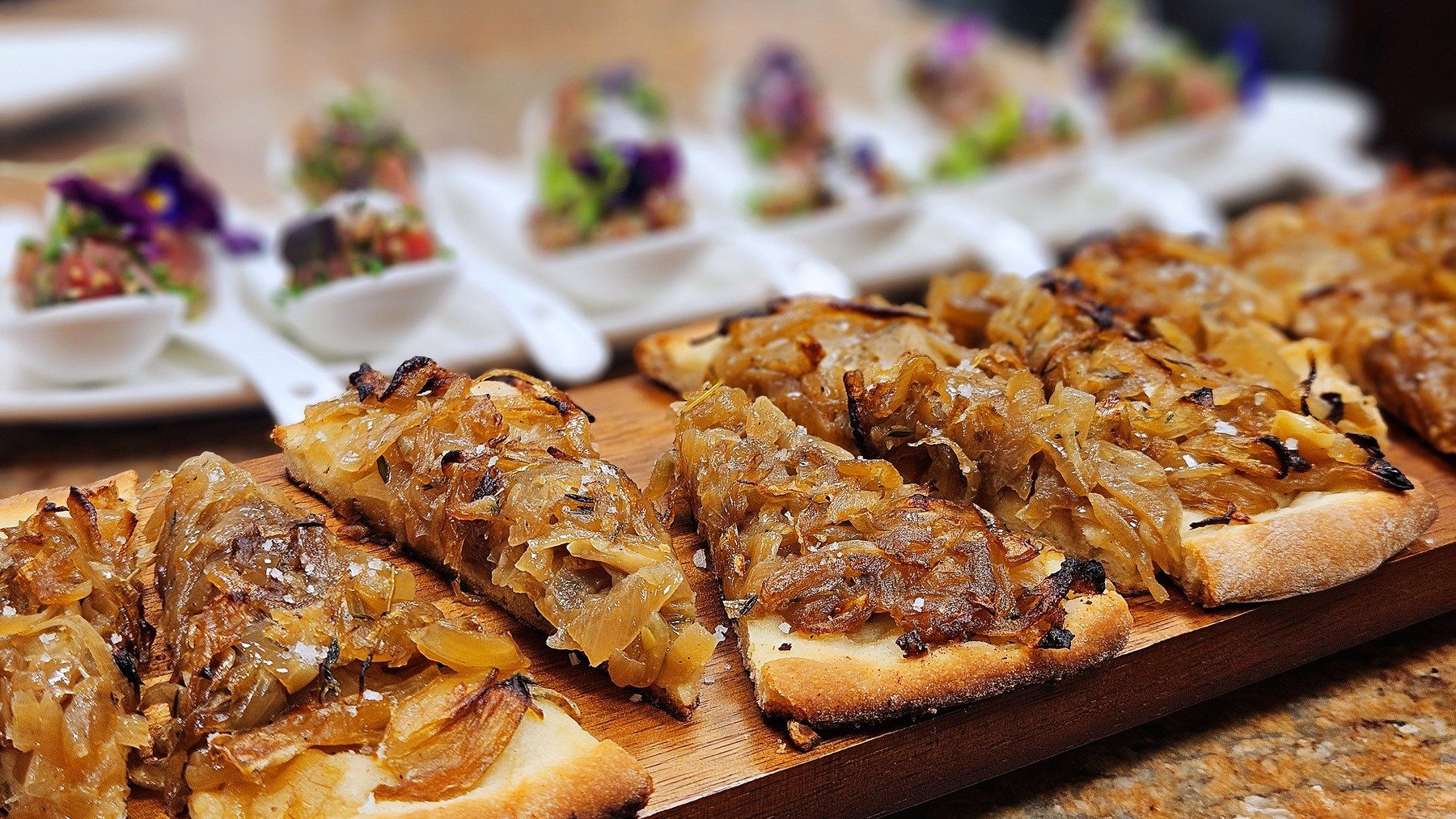 Caramelised-onion tartines on a serving board, amuse-bouche spoons behind.