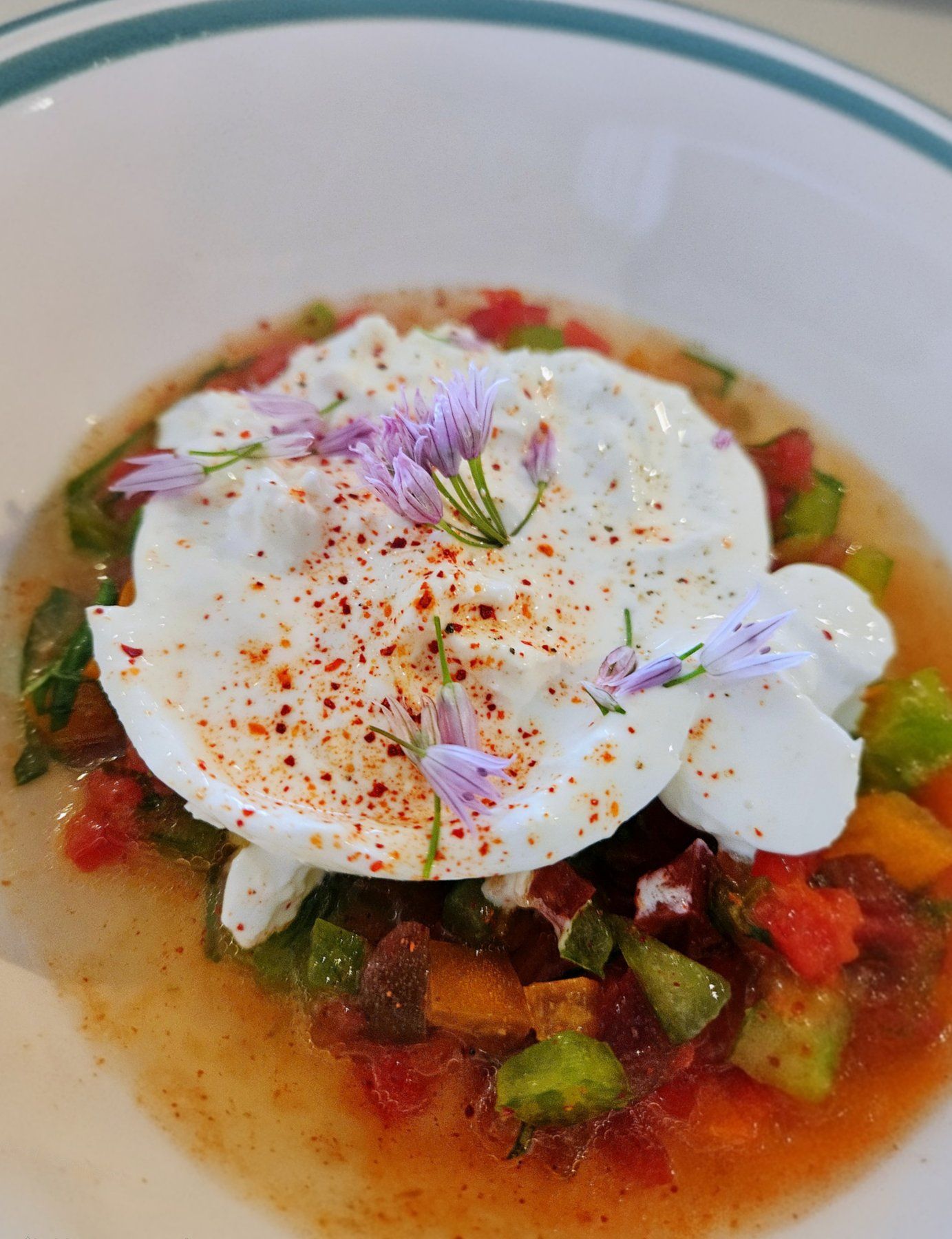 Burrata with tomatoes and chive flowers on a plate.